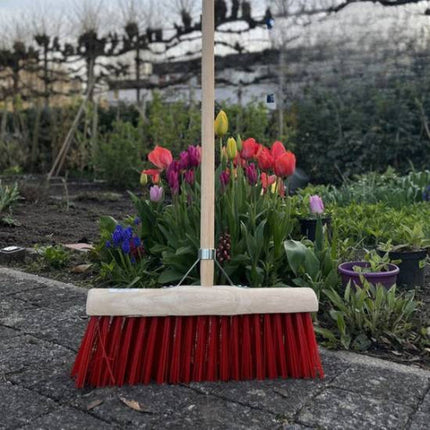 Straatbezem met rode haren in tuin met tulpen